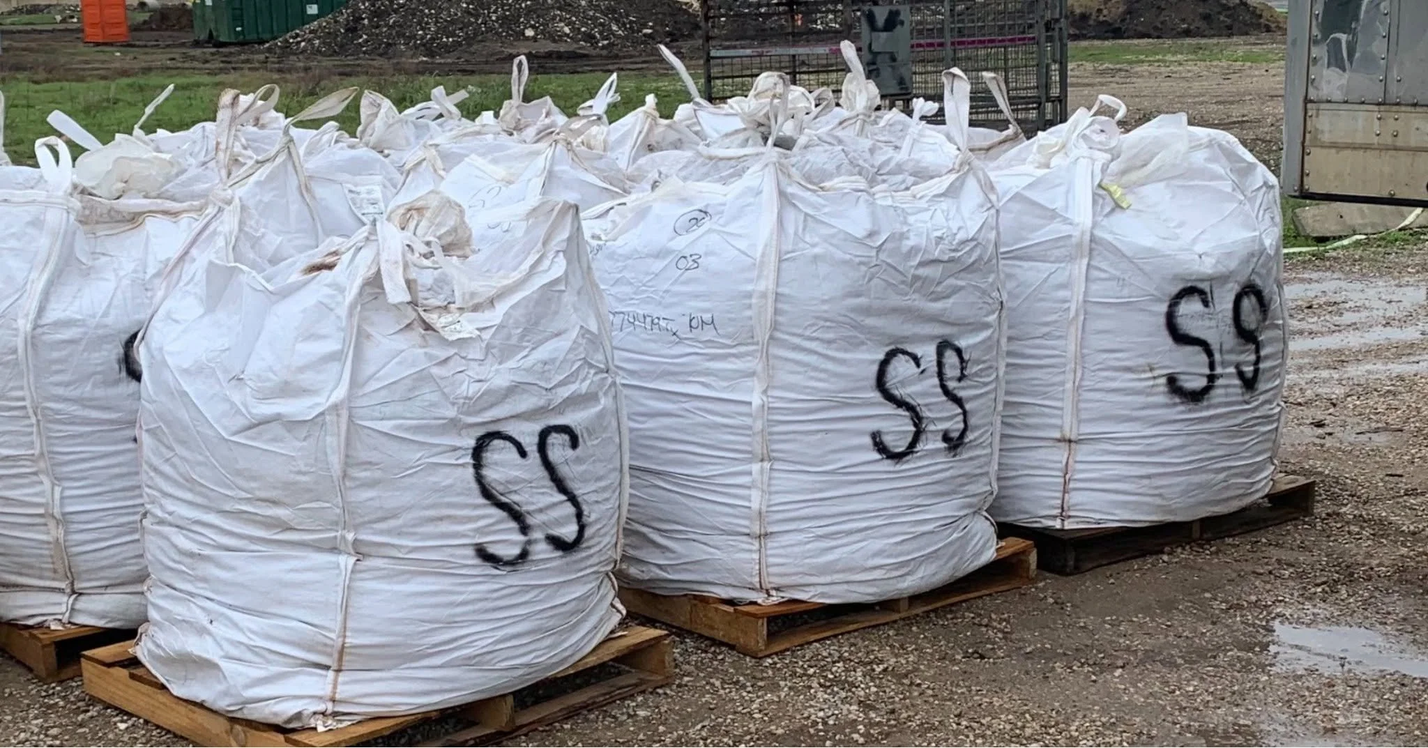 Large white bags with black spray-painted dollars signs on wooden pallets outdoors.