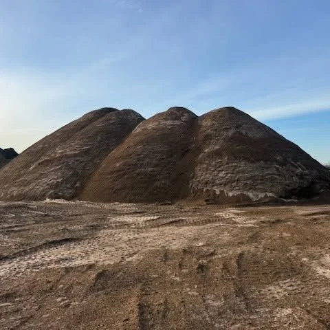 Three large dirt piles or mounds on farm or construction site under a blue sky.