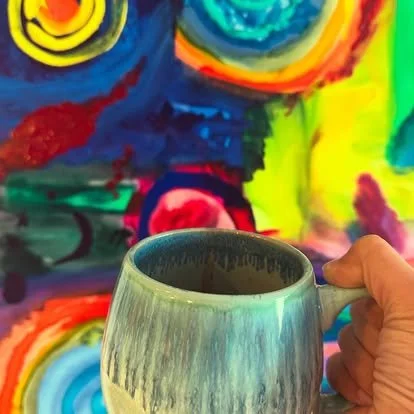 Person holding a mug with a colorful abstract painted wall in the background.