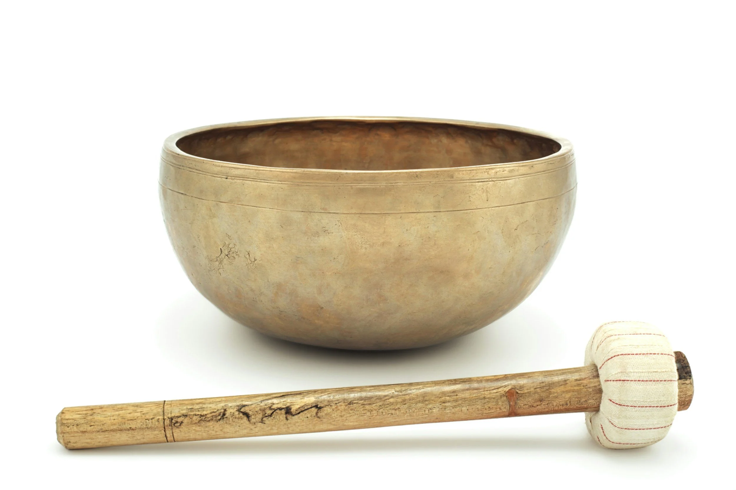 A brass singing bowl, a wooden mallet with a striped cloth handle, and a small beige cloth with red lines on a white background.