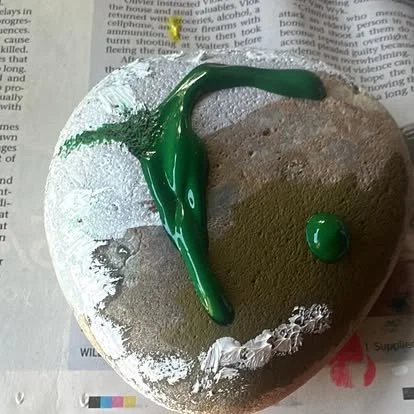 A paint-covered rock with green paint splattered on it, resting on newspaper.