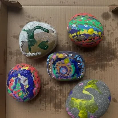 Five painted rocks inside a cardboard box, each with different colorful designs.