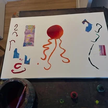 Child's artwork featuring a red octopus with wavy orange legs, colorful scraps, and abstract shapes on white paper.