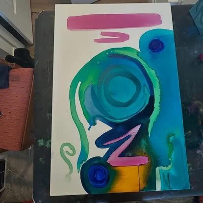 An abstract watercolor painting with a large blue spiral shape surrounded by green, with pink and purple accents, on white paper.