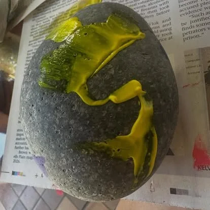 A gray stone with yellow-green paint applied on top, placed on newspaper.