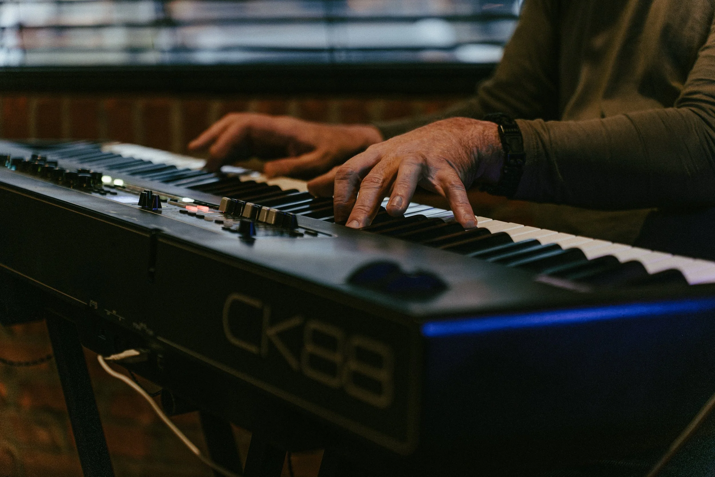 Close-up of a person playing a keyboard, showing their hands, with a background of a window with blinds.