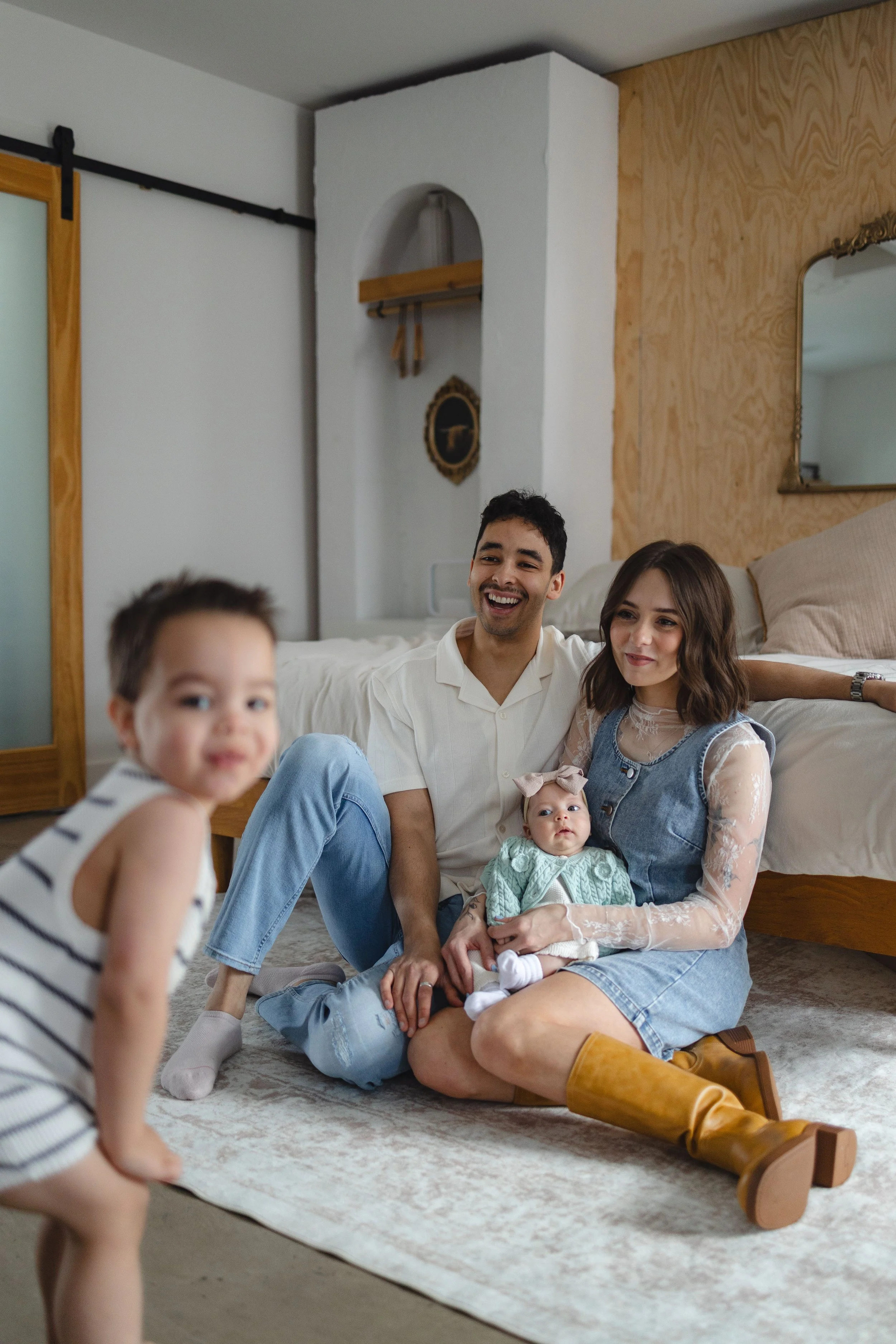 Family sitting on the floor in a cozy bedroom, smiling and enjoying each other's company.