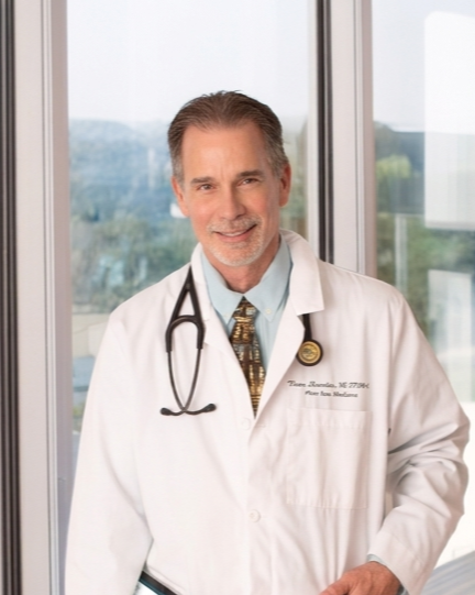 Male doctor in white coat with stethoscope standing in front of windows
