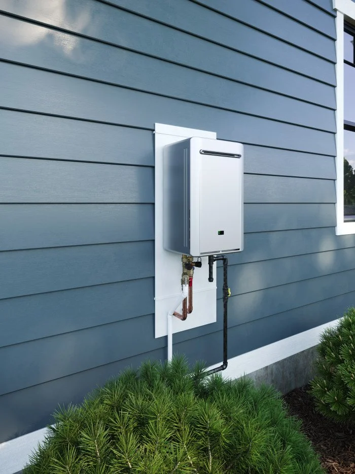 A modern outdoor tankless water heater mounted on a house exterior with blue siding, surrounded by green bushes.
