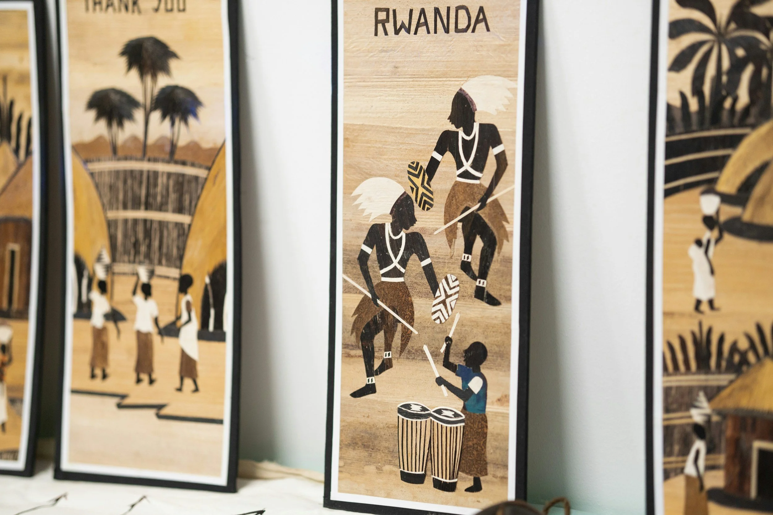Illustration of two women with tribal face paint and traditional clothing playing soccer, with drums at their feet and the word 'Rwanda' at the top.