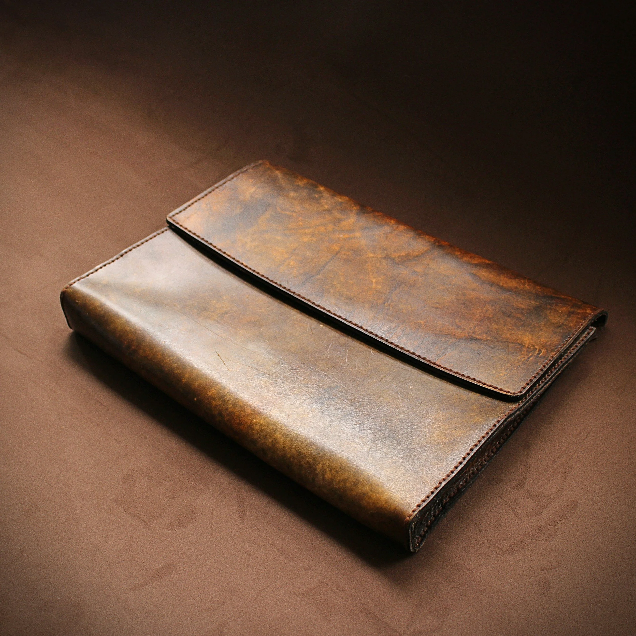 Close-up of a brown leather wallet laying on a flat brown surface with a second piece of material partially visible beneath it.