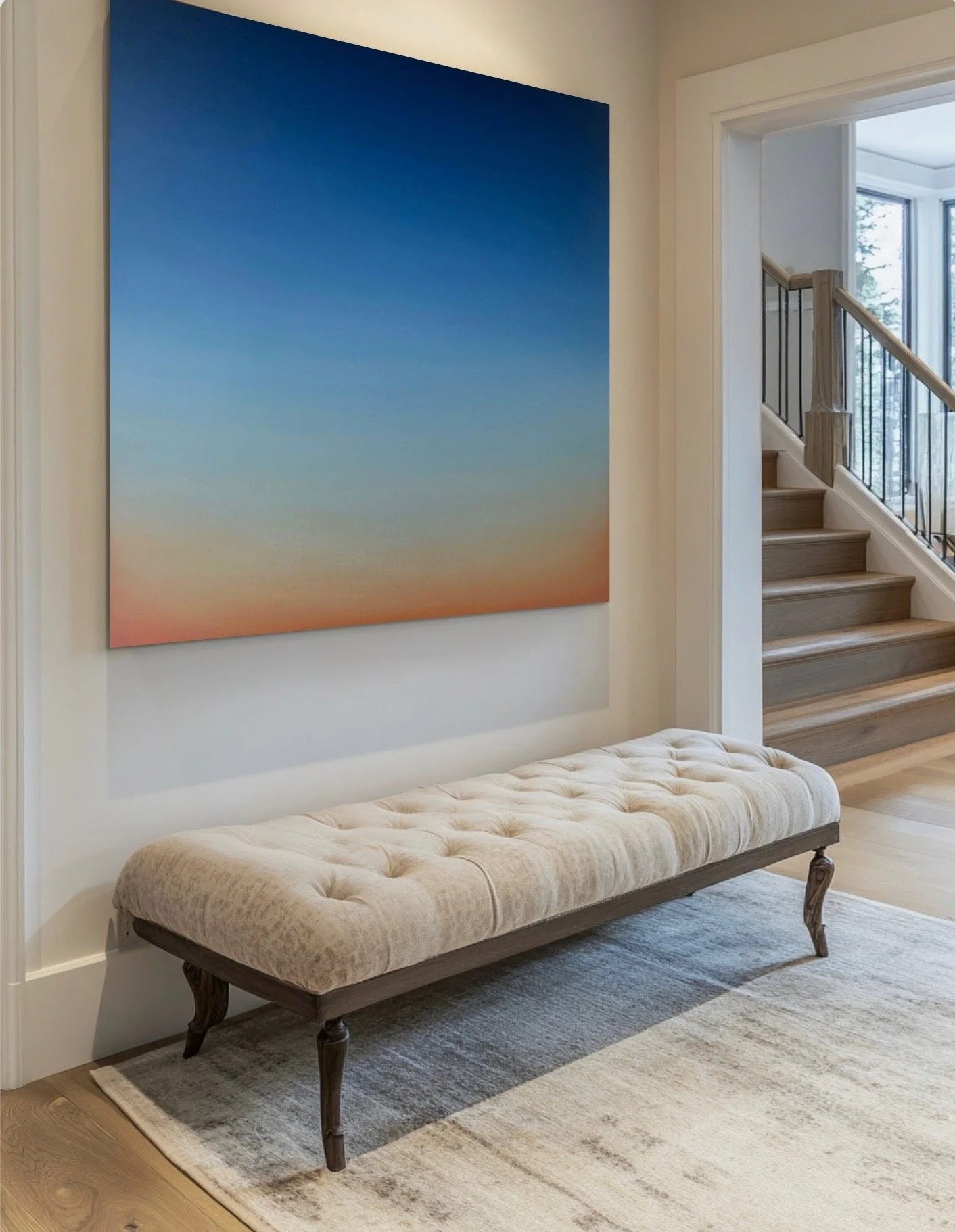 A hallway with a tufted beige bench, a large gradient sunset artwork on the wall, and stairs with wooden steps and black metal railing leading to the upper level, near a large window.
