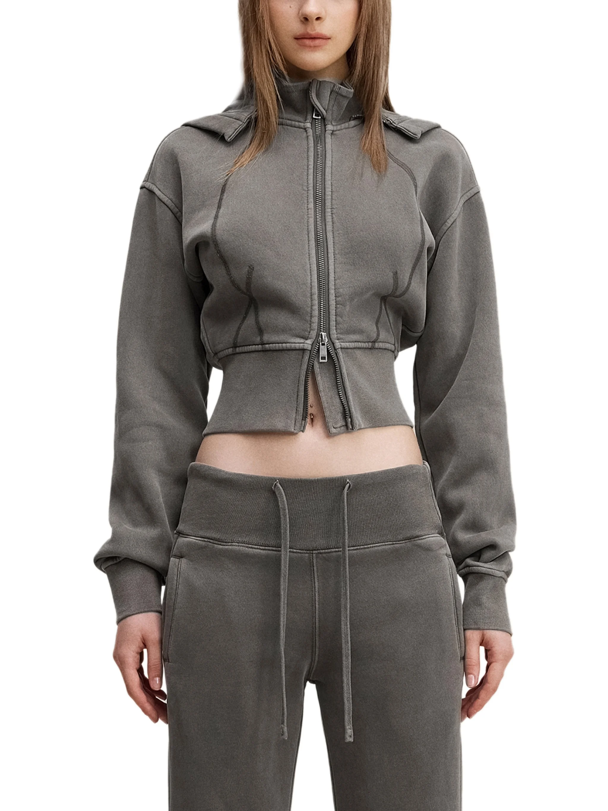 A woman wearing a gray zip-up hoodie and matching gray sweatpants, standing with her arms relaxed by her sides.