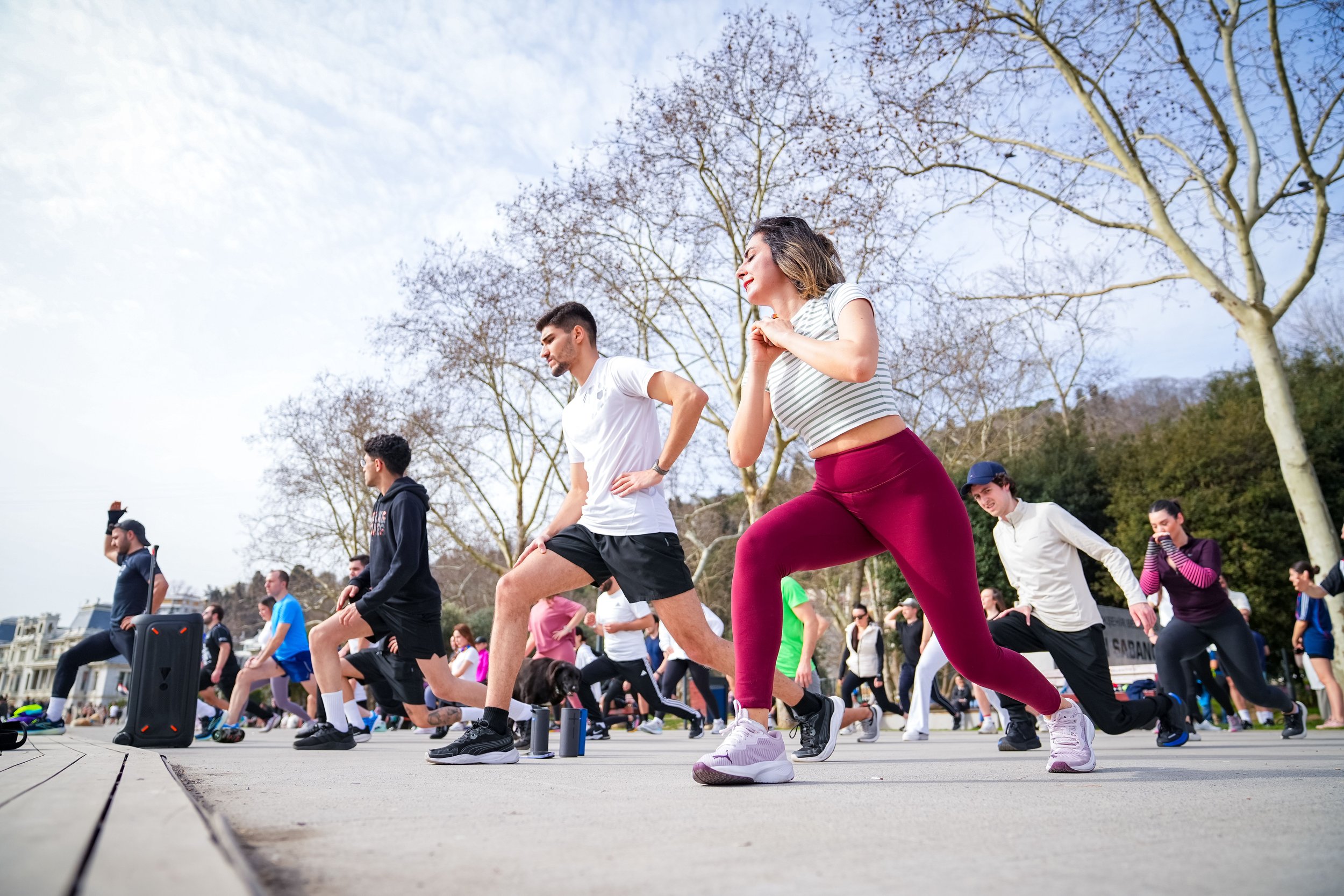 People participating in an outdoor fitness class in a park, doing squats on a wooden platform.
