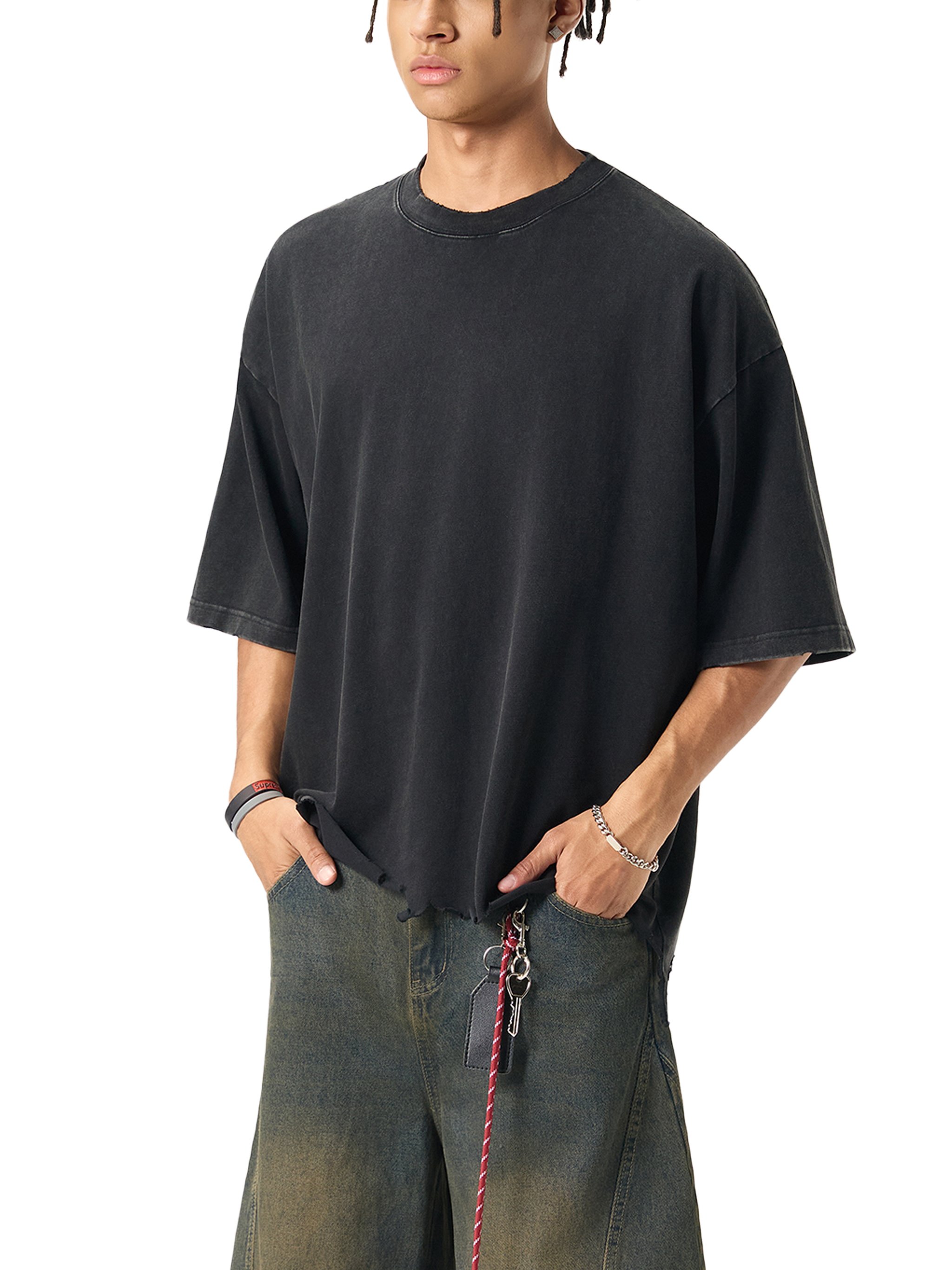 A young man wearing a black oversized T-shirt with short sleeves and a pair of blue jeans. He has a bracelet and rings on his right hand, and a keychain hanging from his belt loop.
