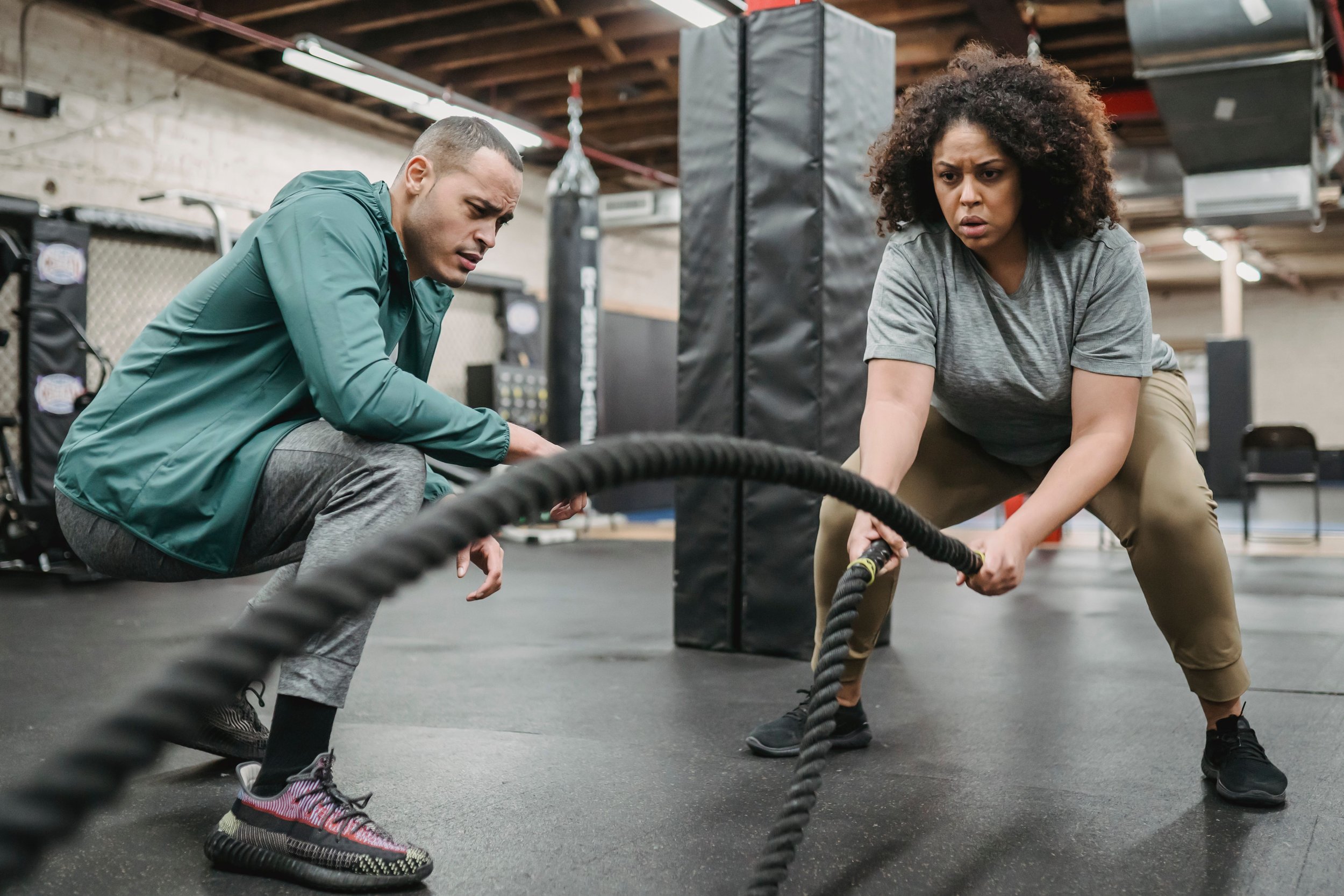 Two women and one man are exercising with battle ropes in a gym, focusing intensely on their workout.