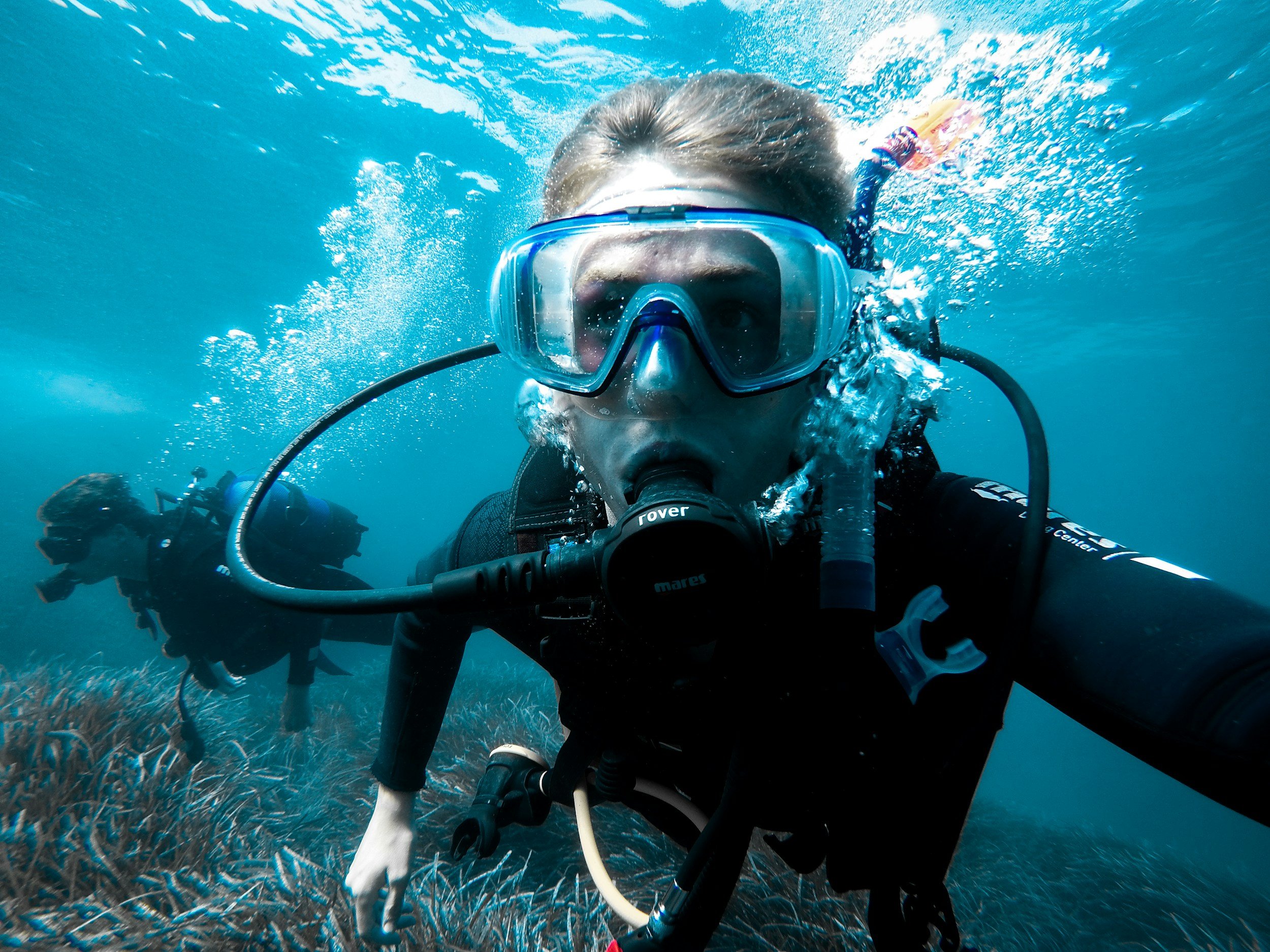 Persona practicando esnórquel en el fondo del océano con equipo de buceo y máscara, rodeada de agua y coloridos peces.
