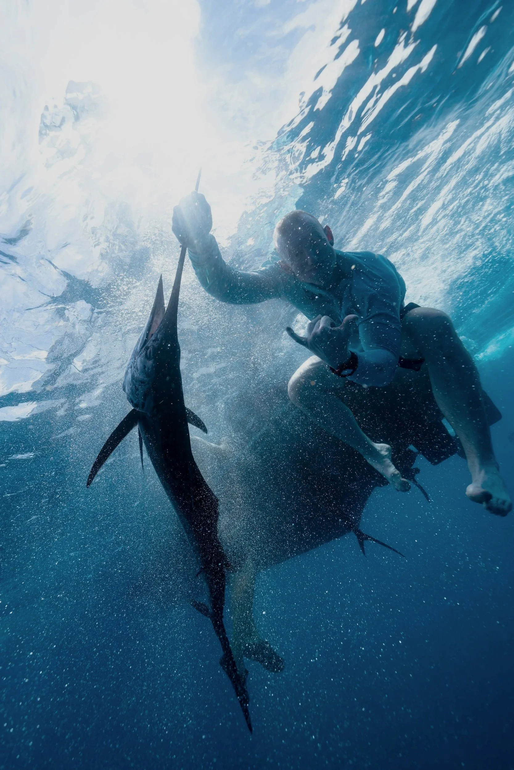 Persona en traje de baño pescando en el océano, rodeada de tiburones, gran cantidad de agua y olas.