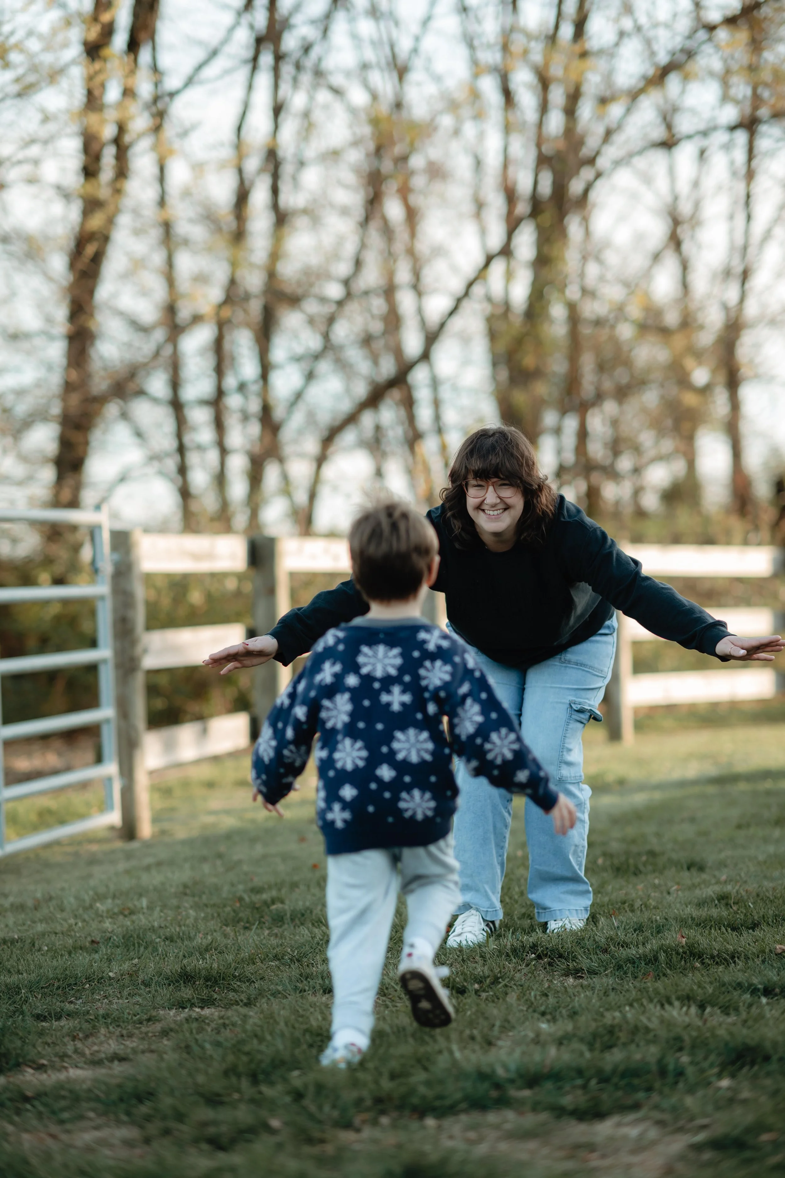 A woman and two children outdoors in a park with trees, playing and enjoying each other's company.