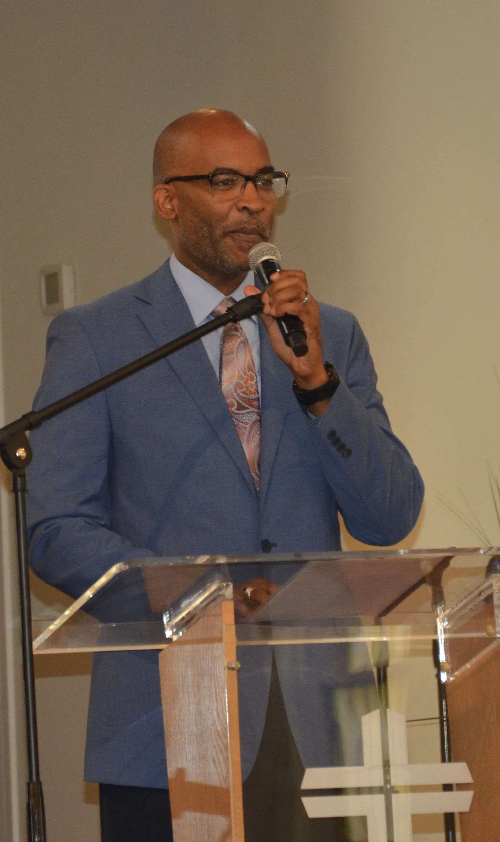 A man in a blue suit and tie speaking into a microphone at a podium.