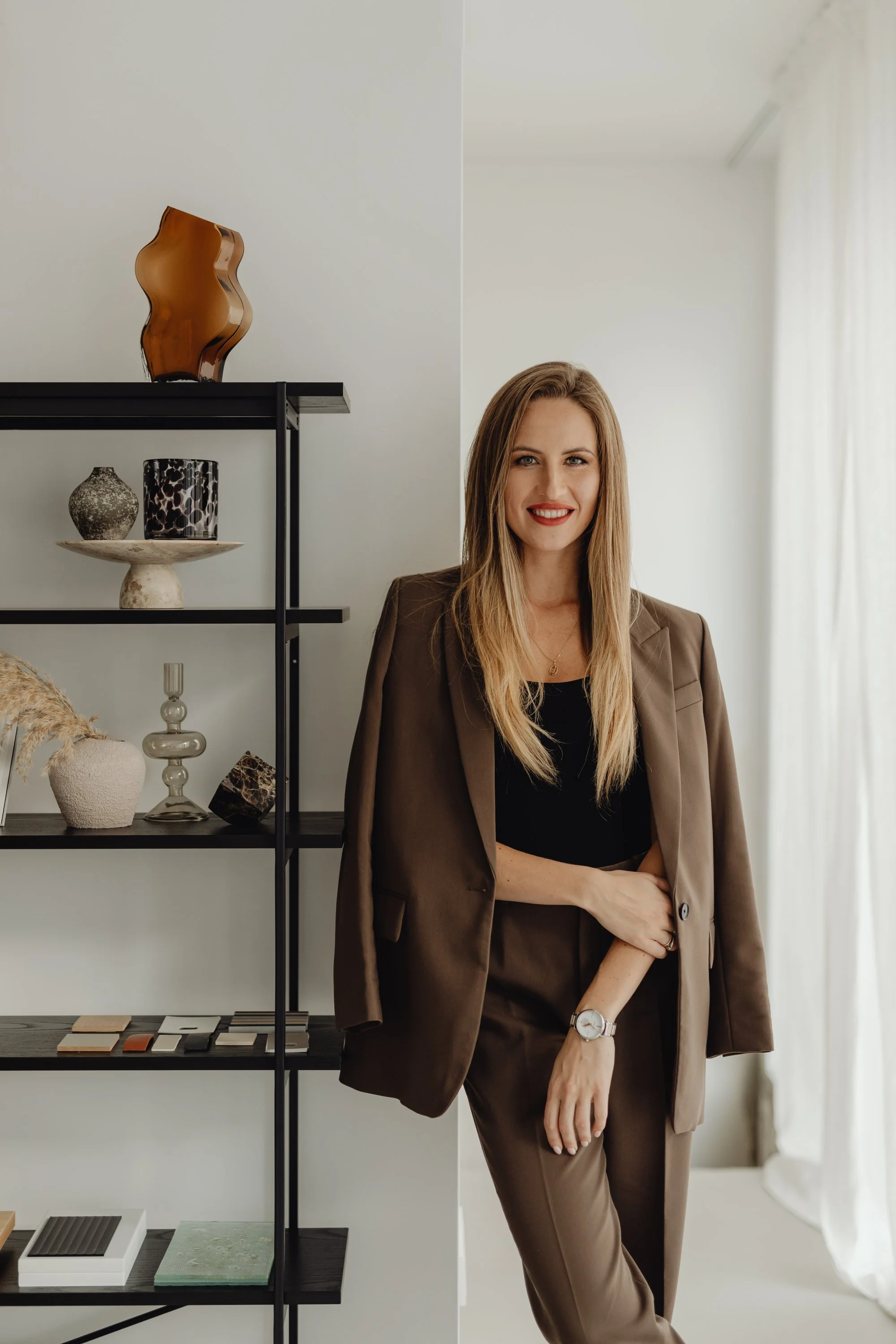 Premium Squarespace Template, Coaching Squarespace Template, Avelã Creative. Woman in brown pantsuit standing beside a shelf with decorative items, including a vase, sculptures, and art pieces, in a well-lit room.