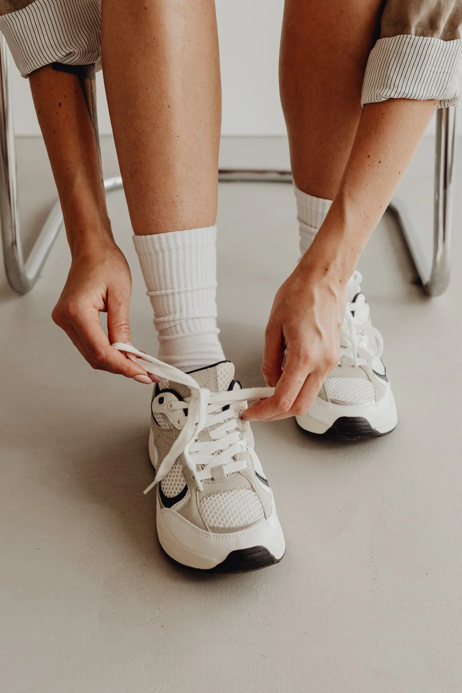 Premium Squarespace Template, Coaching Squarespace Template, Avelã Creative. Person tying white sneakers with white socks and rolled-up pants, sitting on a chair.