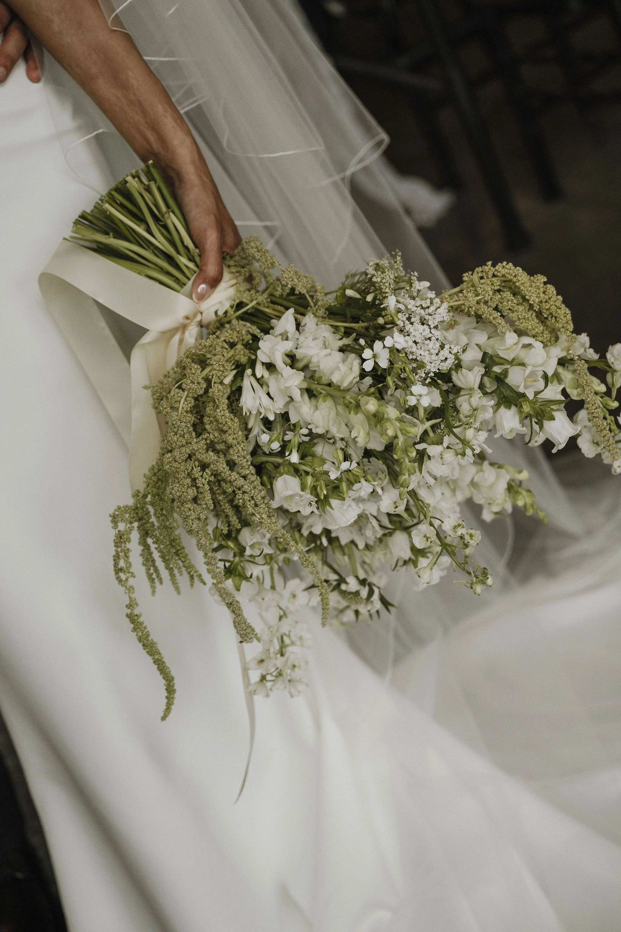 A bouquet of white and green flowers with a satin ribbon is resting on a white surface.