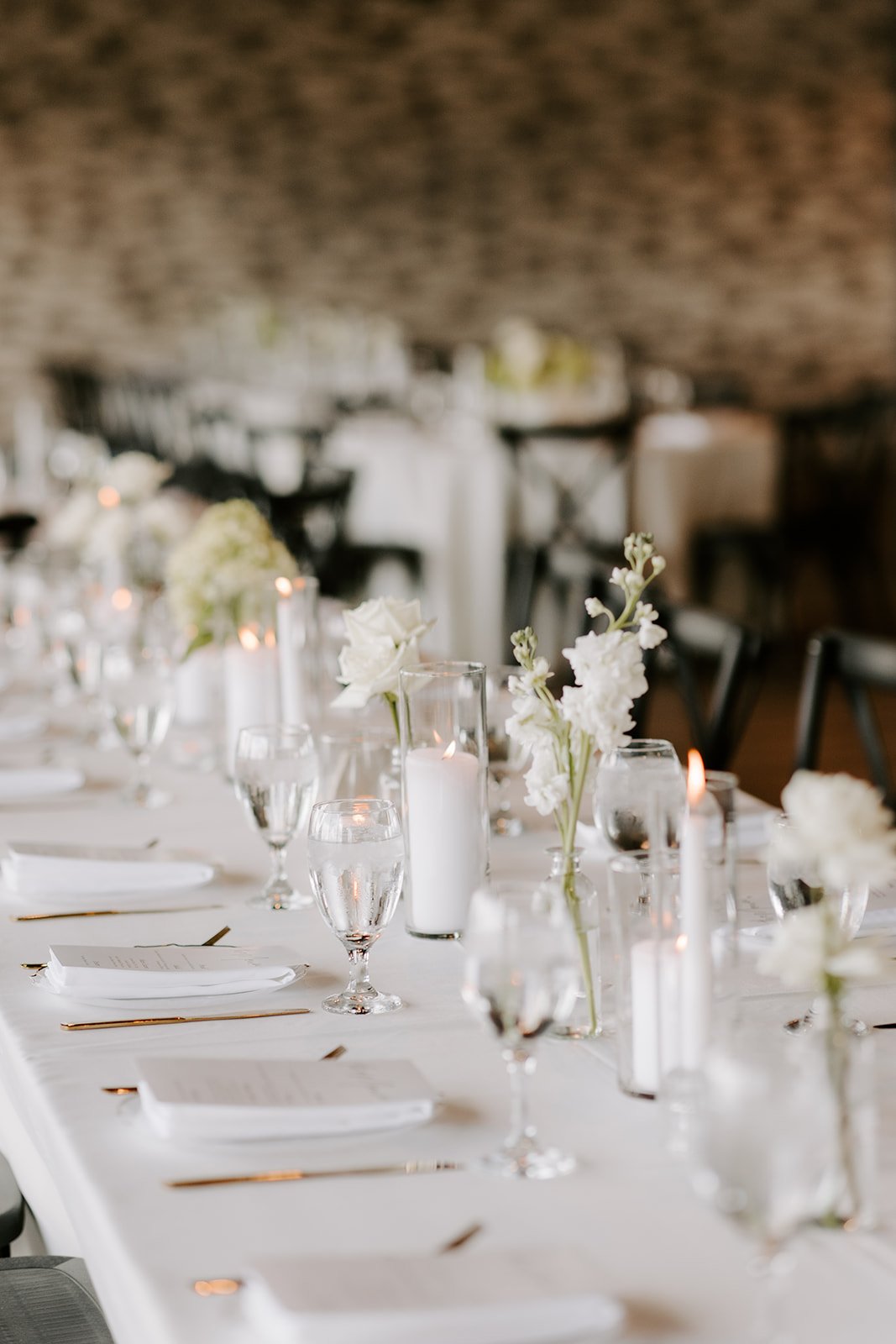 Elegant dining table set with white flowers, candles, glassware, and gold utensils in a decorated event space.