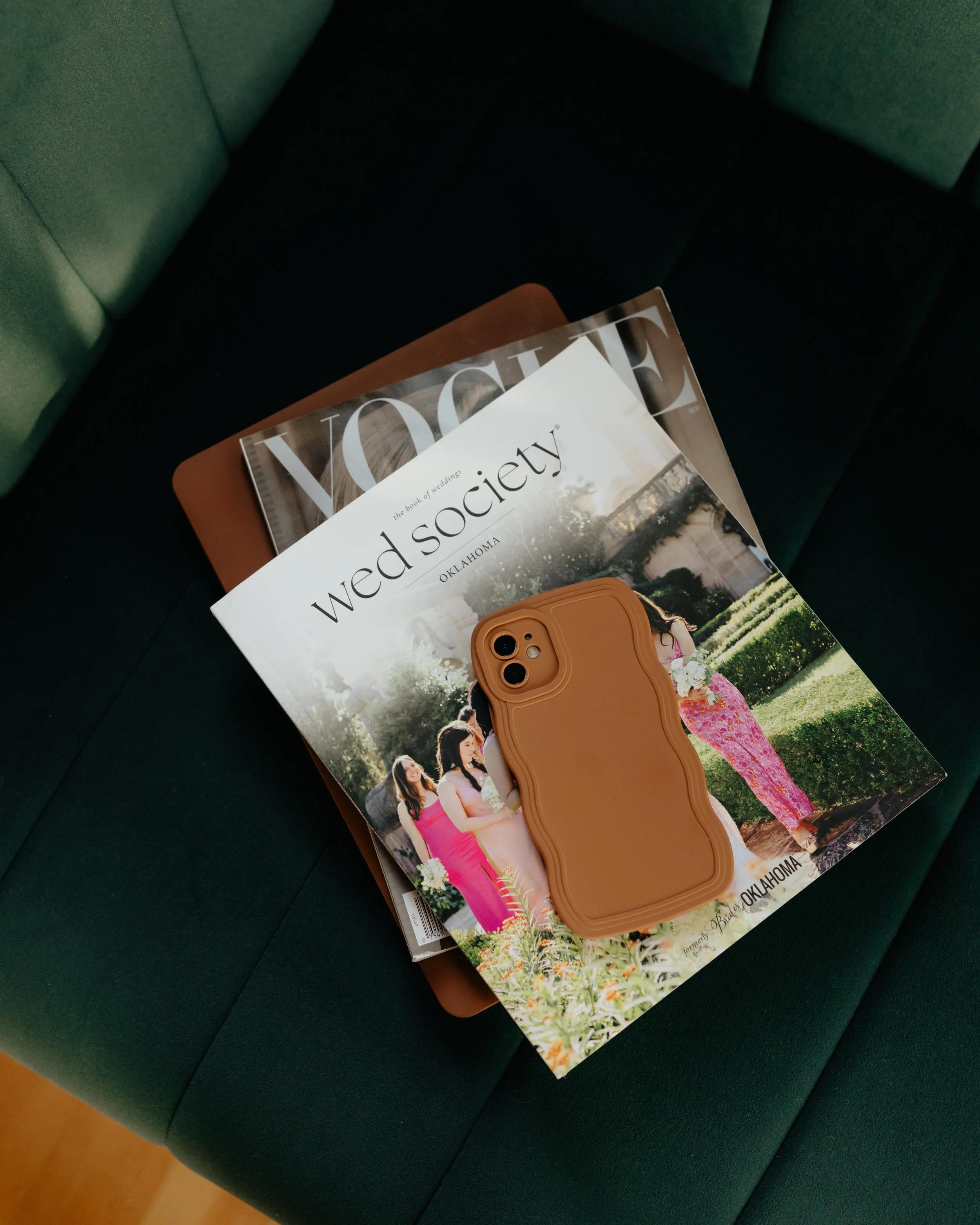 Magazines and a tan phone case on a green couch.