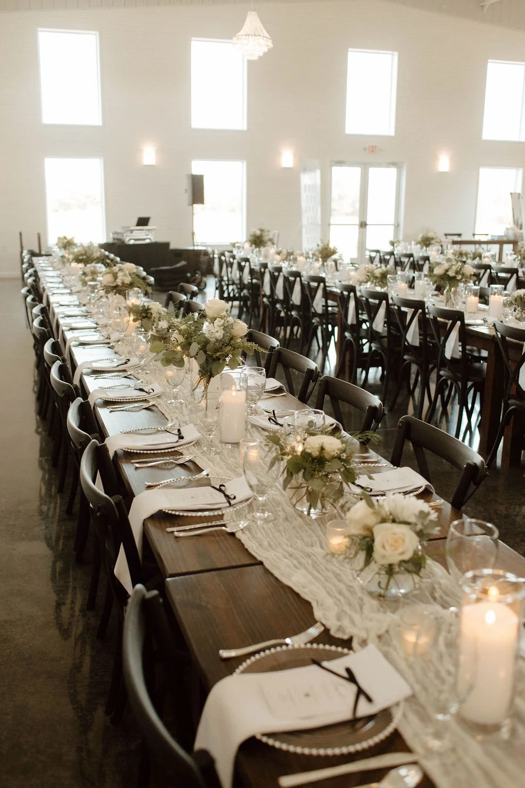 Long banquet table decorated with white flowers, candles, and tableware in a bright, modern event space.