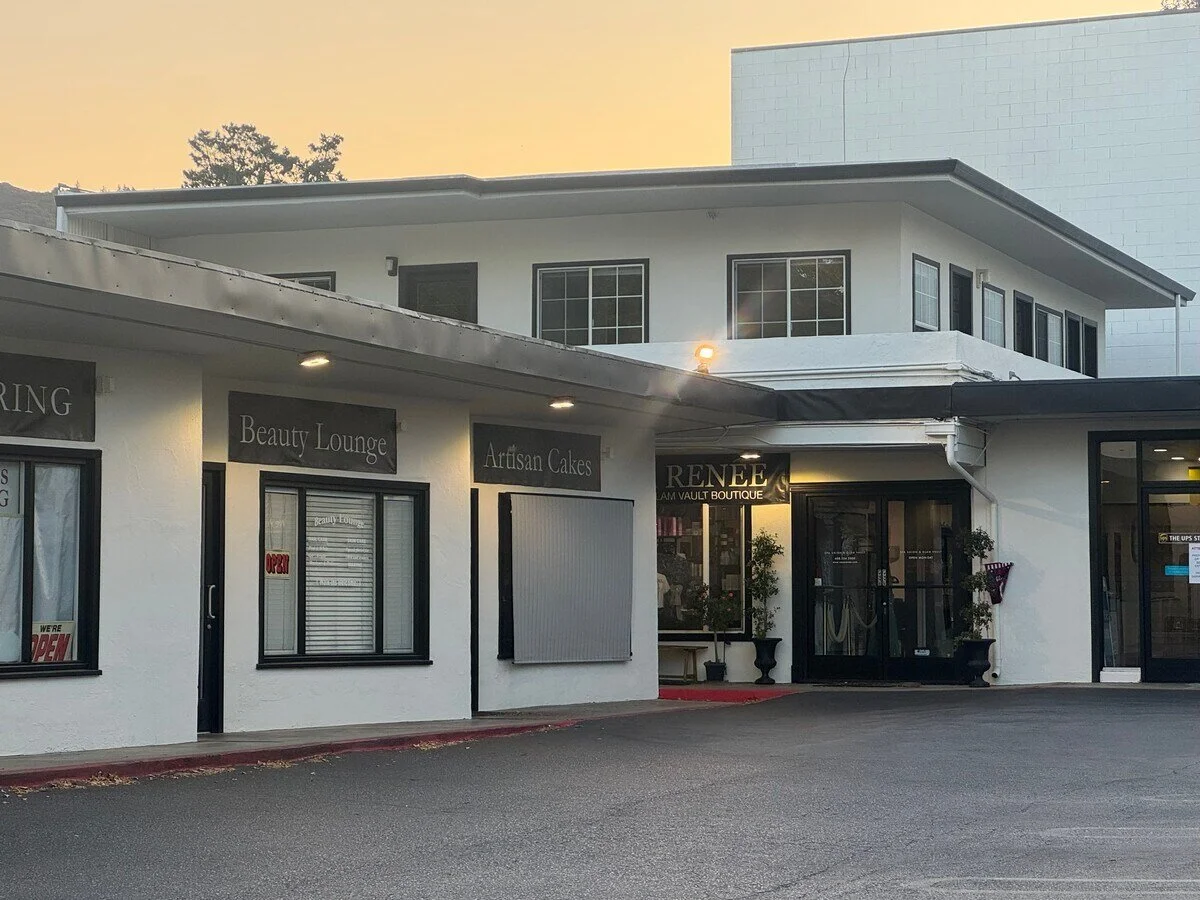 A strip mall with three storefronts: a hair salon, a beauty lounge, and a boutique named Rene, with an apartment building in the background.