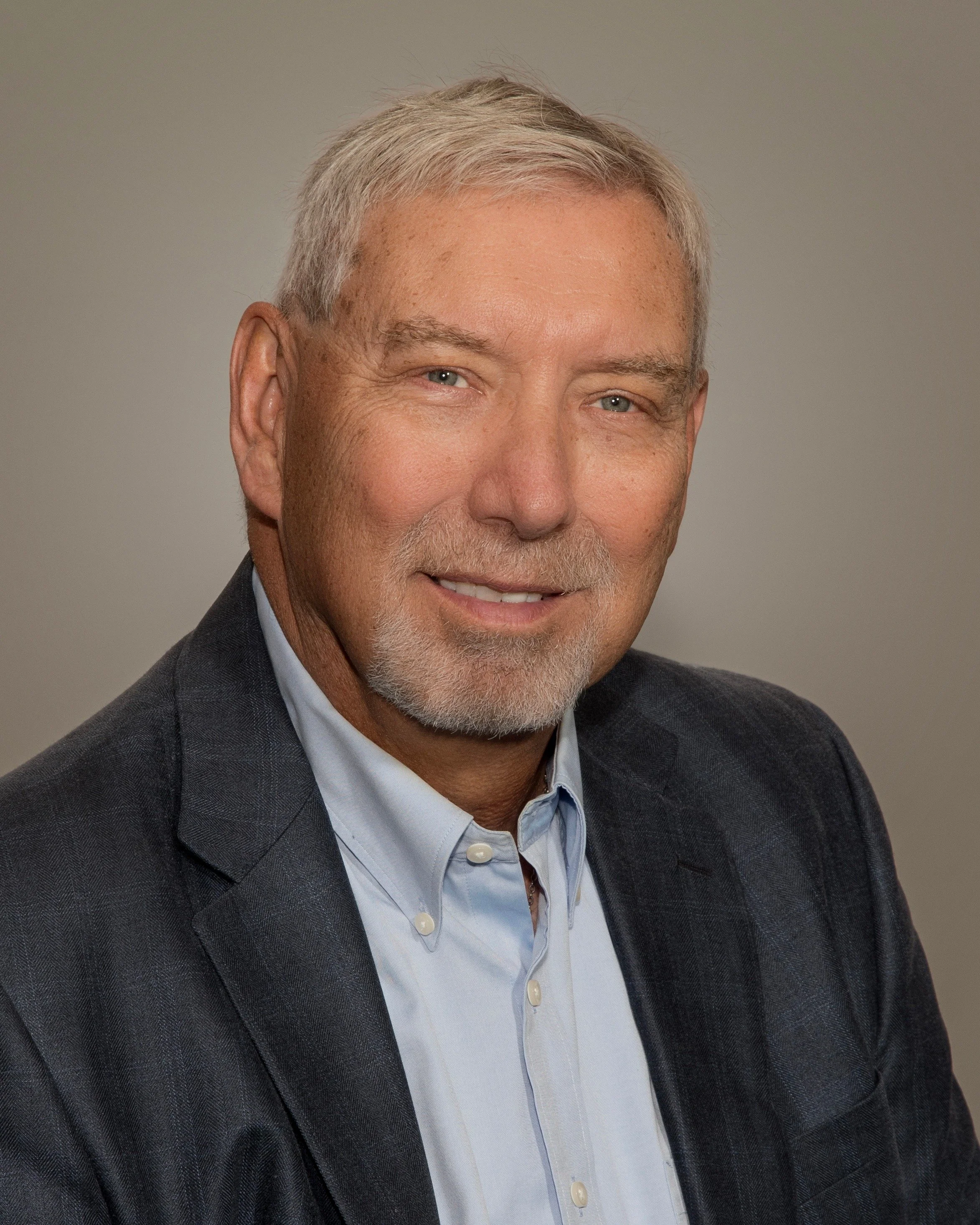 Close-up of smiling mature man with gray hair and beard wearing a suit and open-collared shirt.