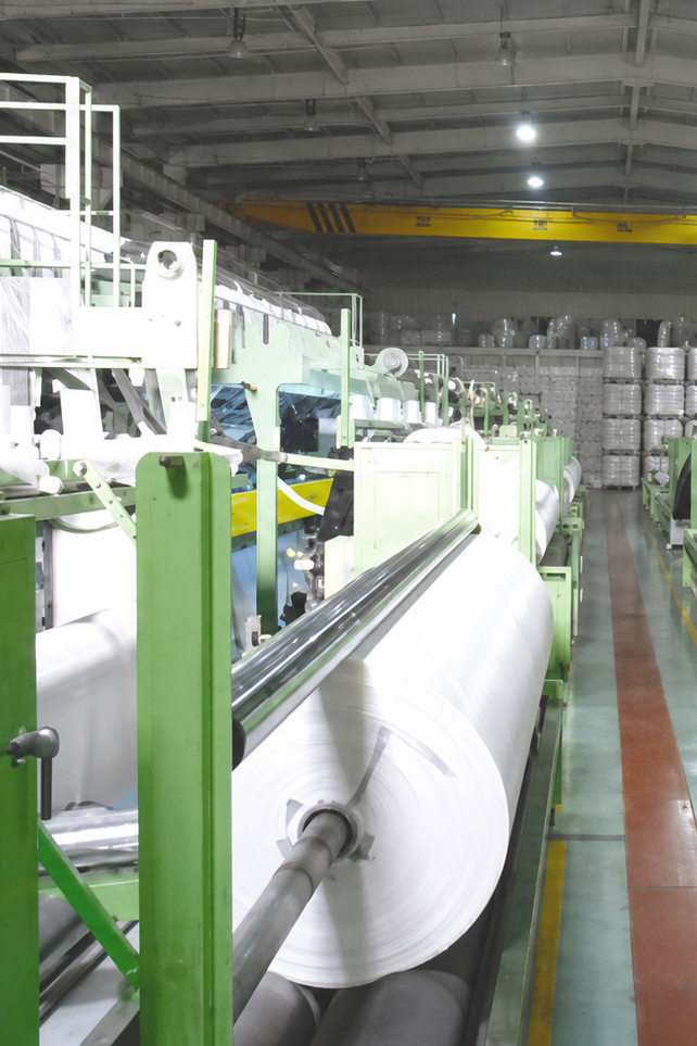 Industrial manufacturing facility with large rolls of white material on a machine