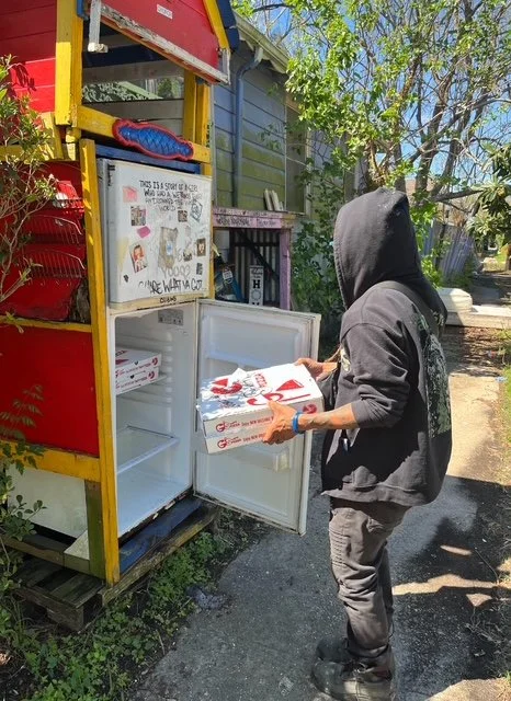 Songbird Renovations founder filling a community fridge with pizza.