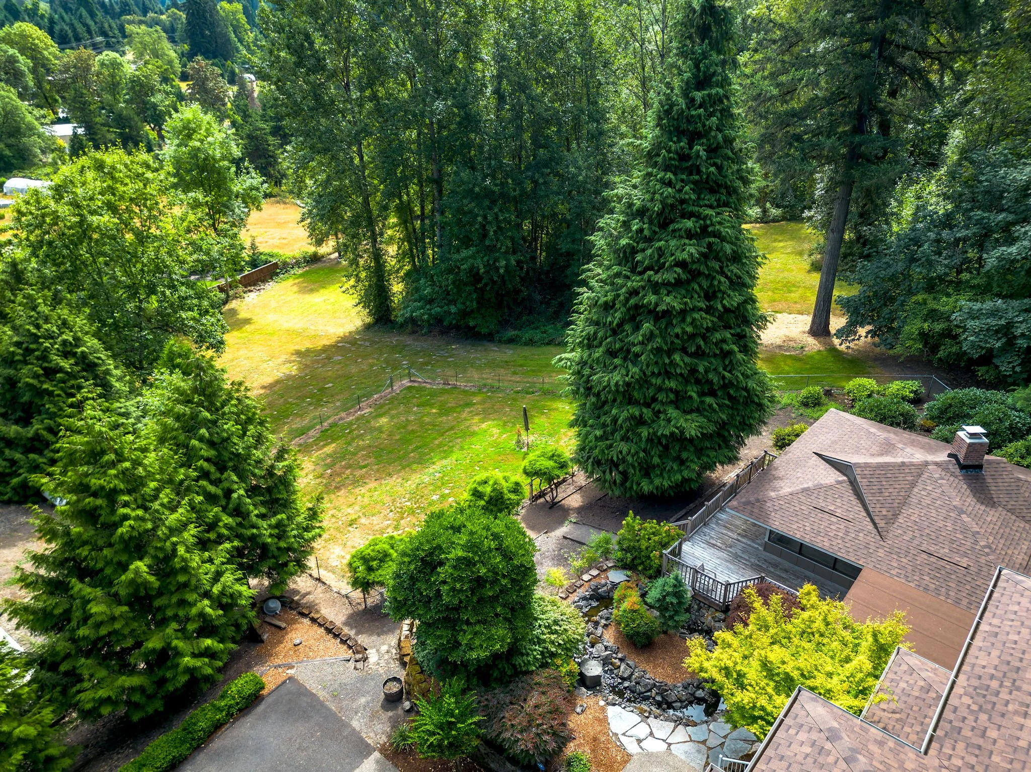 Image of roof of cottage, wooden deck, tall green trees and grass