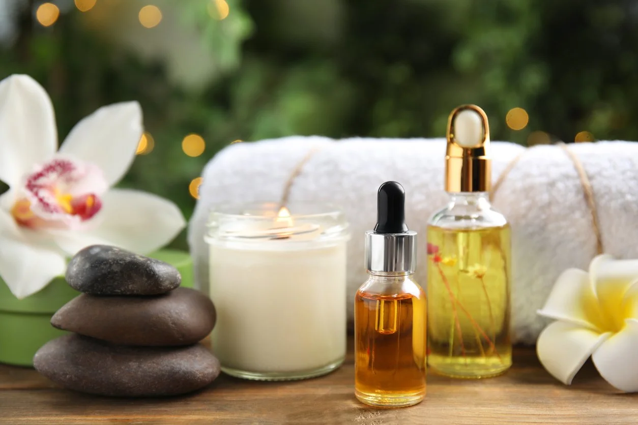Spa setup with essential oils, rolled white towel, candles, stones, and flowers