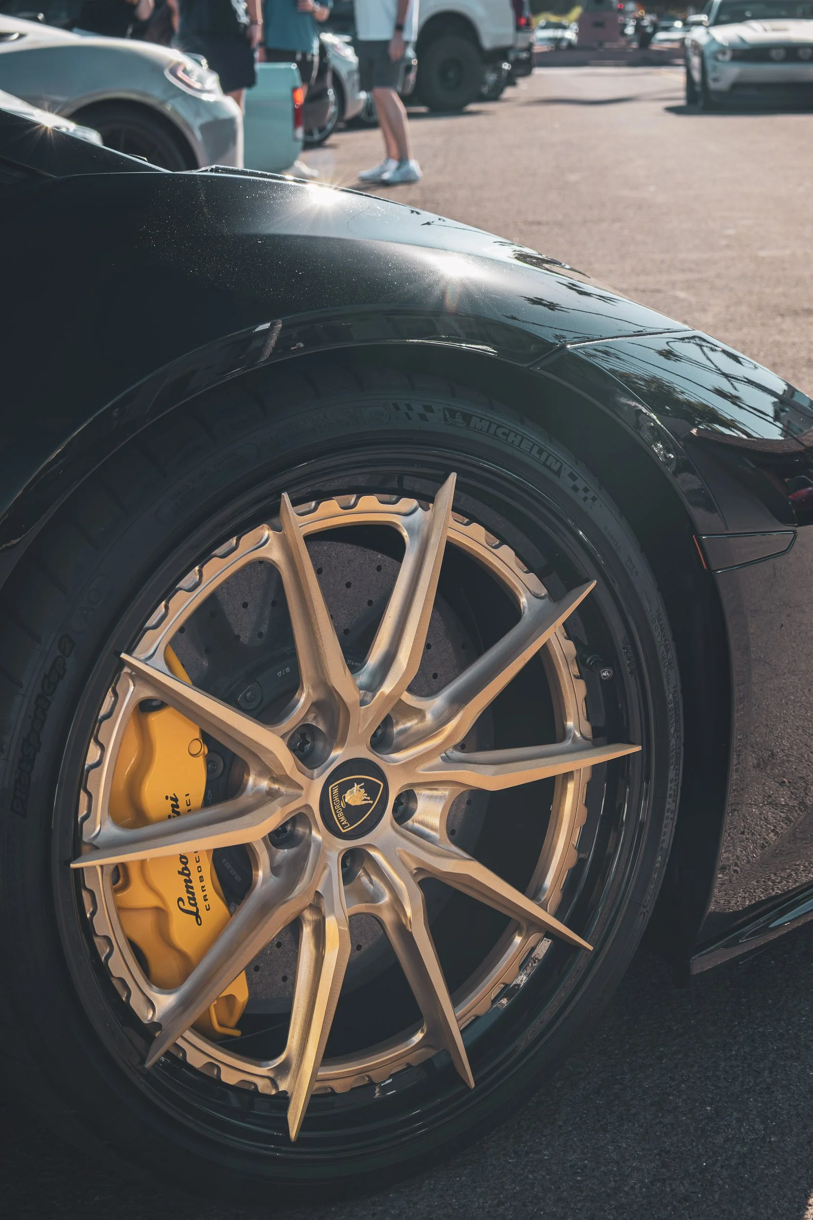 Macro detail exotic car photography focusing on the aggressive bronze multi-spoke wheel, yellow Lamborghini carbon ceramic brake caliper, and sleek black paint of an Italian supercar during a cars and coffee event in Scottsdale, Arizona, captured by 