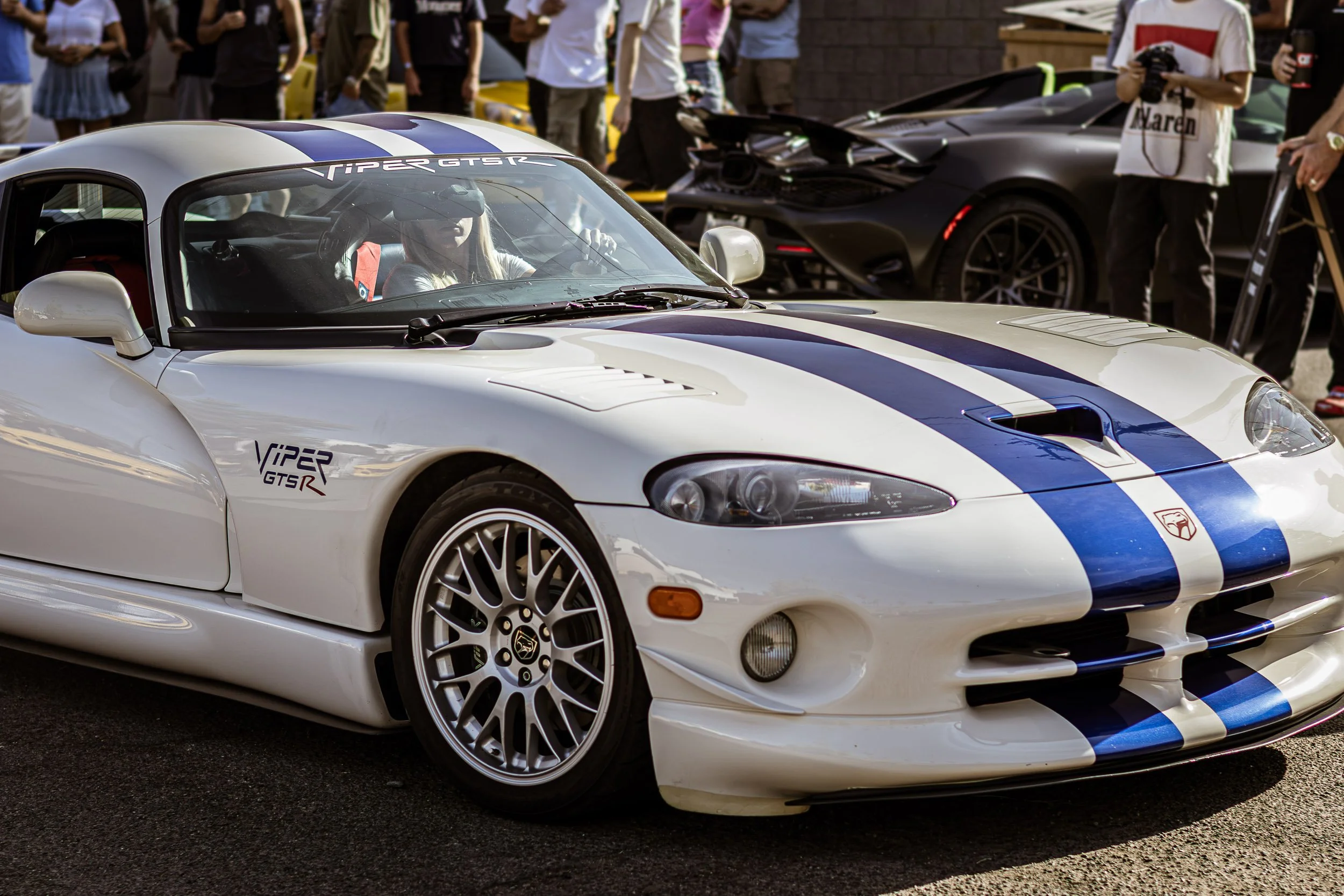 Dynamic front three-quarter automotive photography featuring a classic white Dodge Viper GTS-R with blue racing stripes rolling through a lively car meet crowd in Scottsdale, Arizona, captured by Curtis from Gasoline and Dopamine.