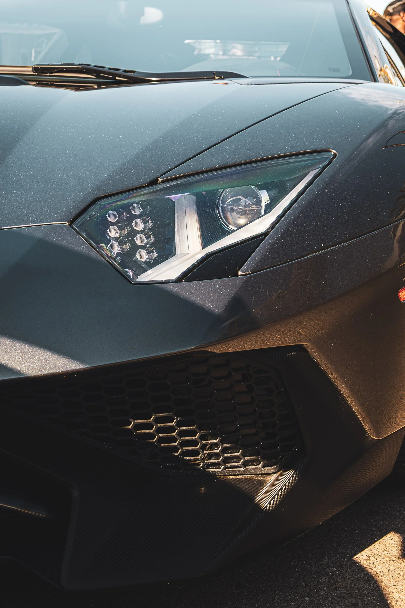 Macro detail automotive photography highlighting the angular LED headlight and hexagonal lower grille of a black Lamborghini Aventador LP 700-4 in Gilbert, Arizona, captured by Curtis from Gasoline and Dopamine.