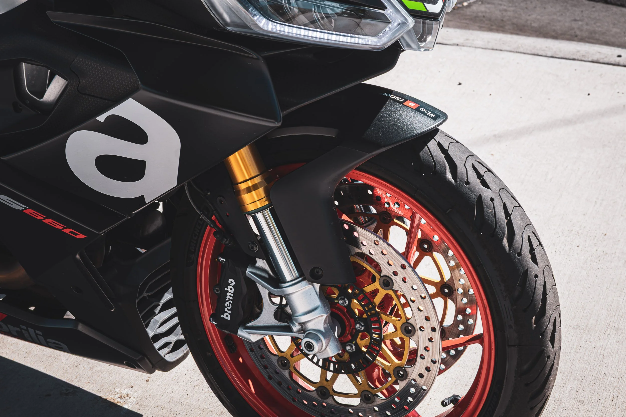 Macro detail motorcycle photography focusing on the striking red wheel, Brembo brakes, and matte black fairing of an Aprilia RS 660 sportbike in Chandler, Arizona, photographed by Curtis from Gasoline and Dopamine.