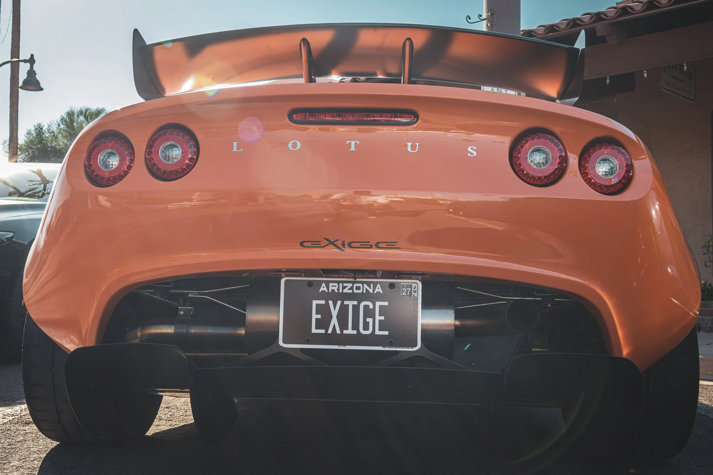 Macro automotive detail photography focusing on the rear fascia, round LED taillights, and prominent rear wing of a vibrant orange Lotus Exige with an Arizona vanity plate, captured by Curtis from Gasoline and Dopamine Car Photography.