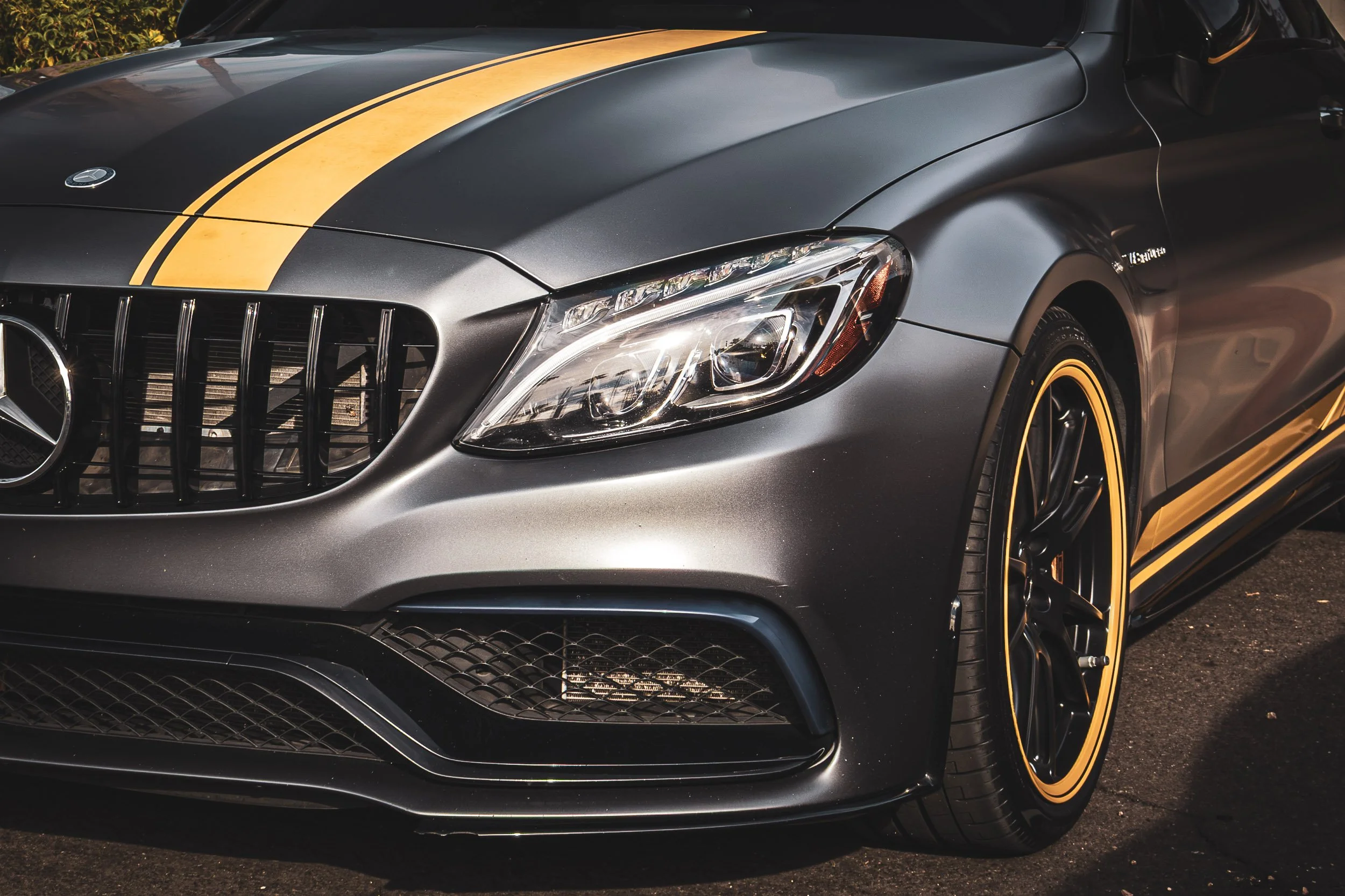 Close-up front quarter automotive photography highlighting the aggressive grille, satin gray paint, distinctive yellow racing stripes, and yellow wheel accents of a Mercedes-AMG C63S Edition 1 in Arizona, captured by Curtis at Gasoline and Dopamine.