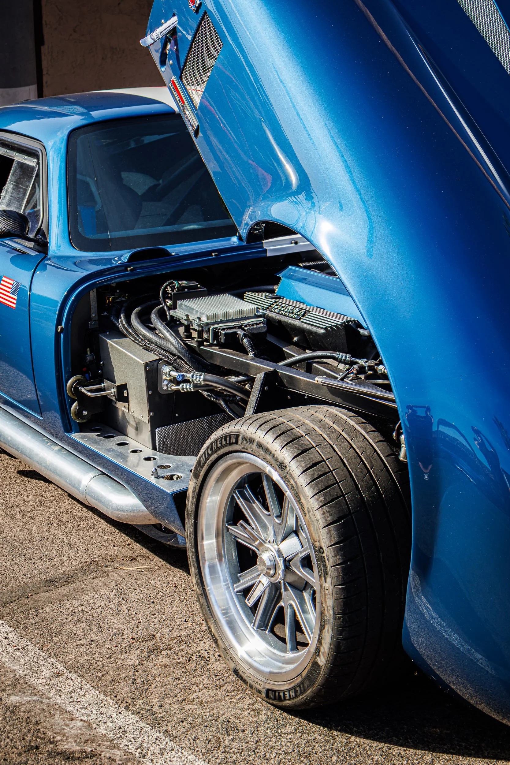 Detailed automotive photography showcasing the open hood, exposed engine bay, and aggressive side-exit exhaust pipes of a classic blue and white Shelby Cobra in Arizona, captured by Curtis from Gasoline and Dopamine Car Photography in Scottsdale.