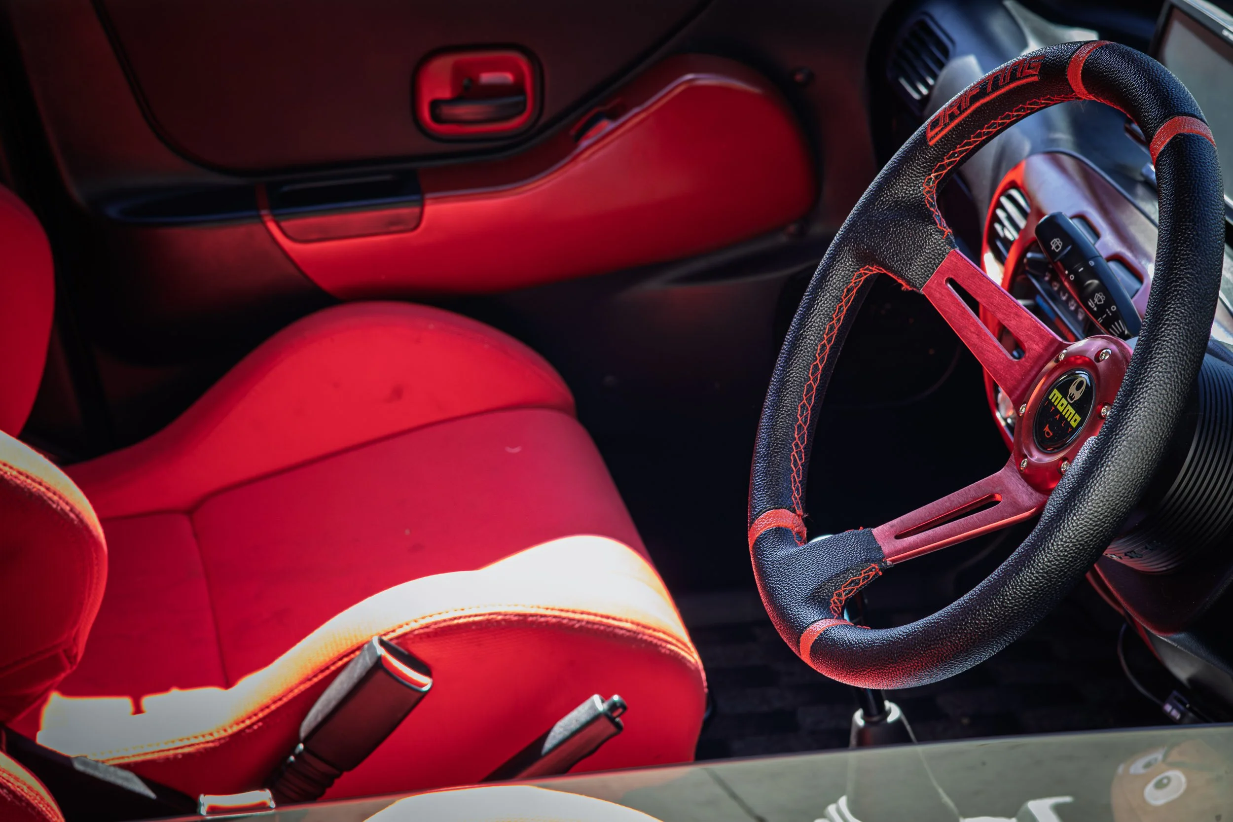 Detail car photography of a custom JDM right-hand-drive interior featuring a red MOMO steering wheel, red racing bucket seat, and custom trim in Scottsdale, Arizona, shot by Curtis from Gasoline and Dopamine photography.