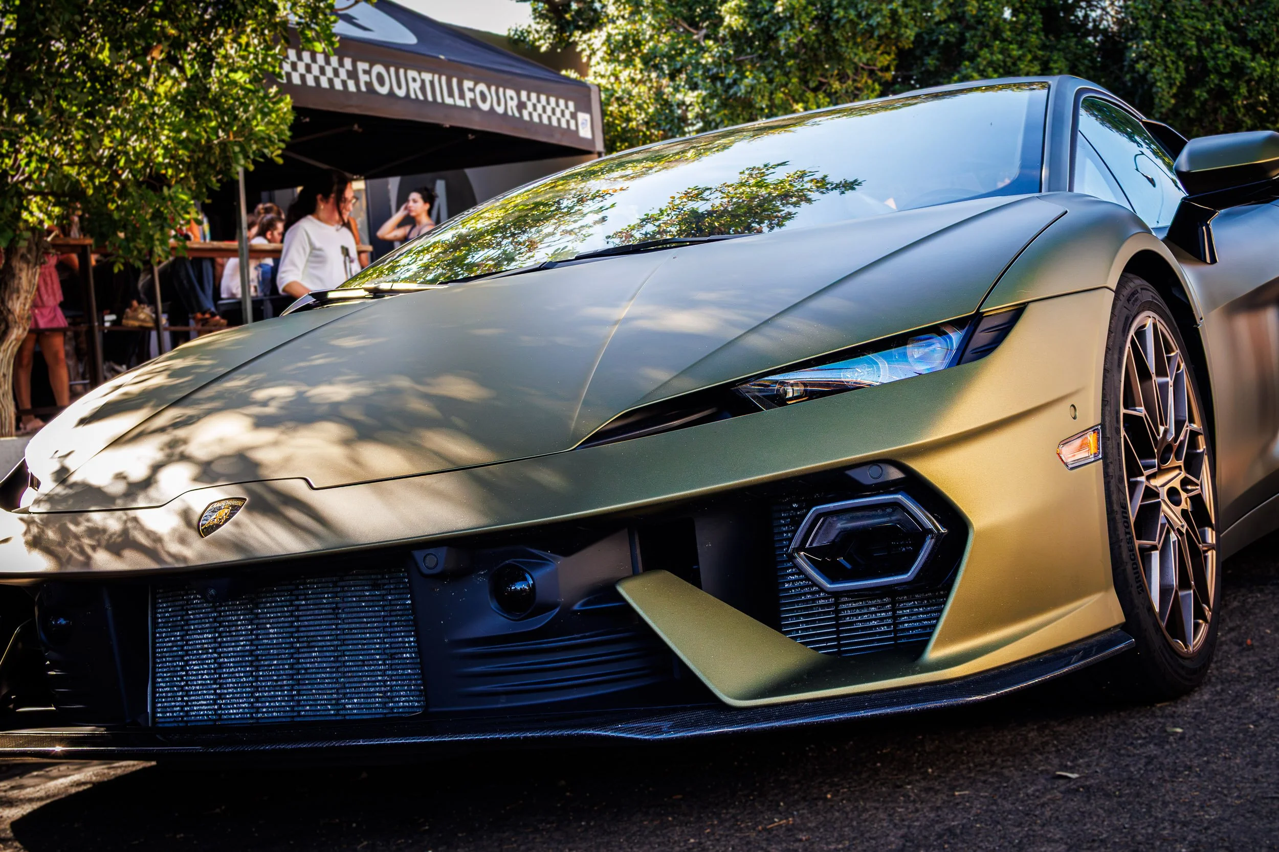 Low-angle front automotive photography showcasing a matte green Lamborghini Temerario featuring bronze wheels, a carbon fiber splitter, and distinctive hexagonal running lights, parked at the Fourtillfour Cars and Coffee event in Scottsdale, Arizona,