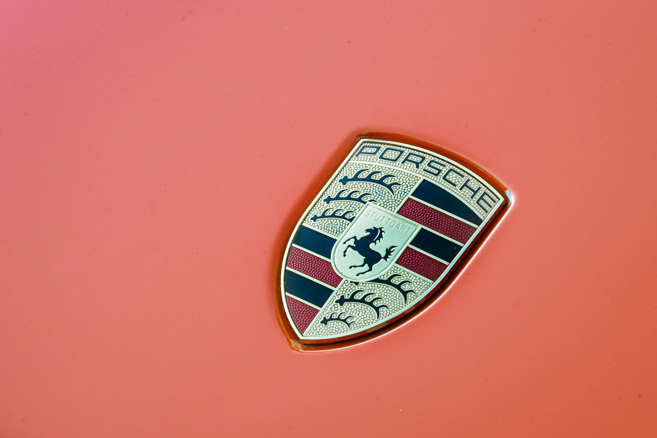 Macro detail car photography focusing on the iconic gold, red, and black Porsche crest hood badge set against Lava Orange paint in Queen Creek, Arizona, captured by Gasoline and Dopamine.