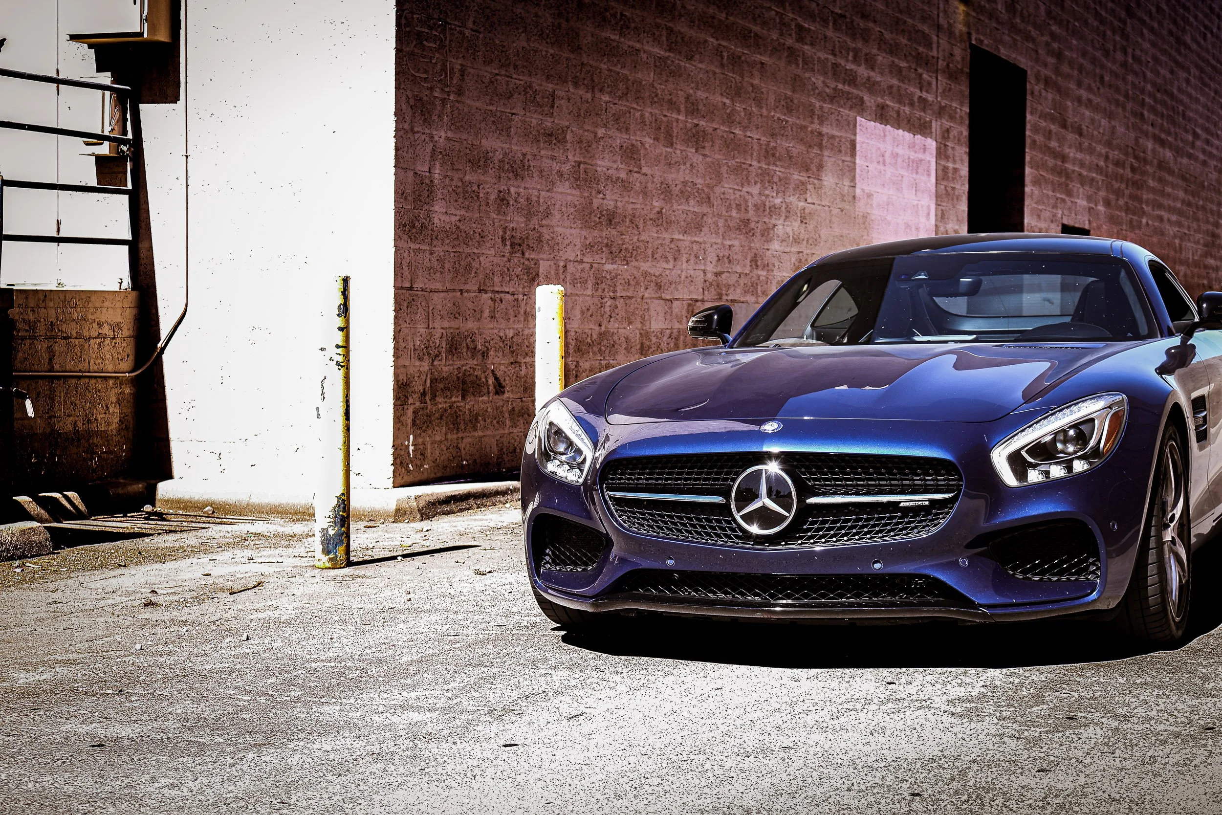 Low-angle front three-quarter automotive photography featuring a metallic blue Mercedes-AMG GT S parked in a textured industrial alleyway under harsh midday sunlight in Queen Creek, Arizona, photograph by Gasoline and Dopamine Car Photography.