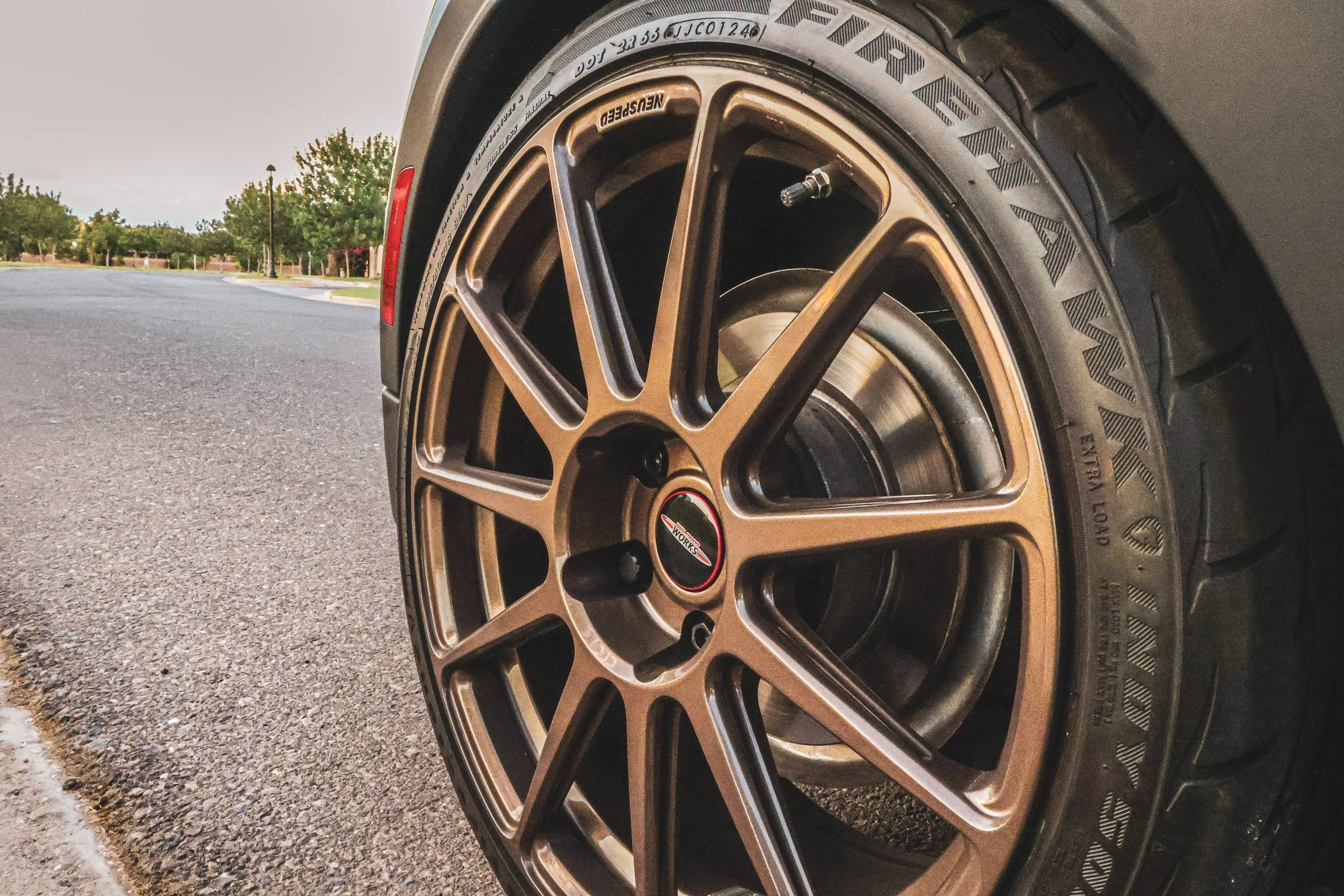 Macro detail automotive photography focusing on a bronze Neuspeed forged wheel, Firehawk Indy 500 tire, and John Cooper Works center cap on a modified Zesty Yellow Mini Cooper, shot at street level in Morrison Ranch, Gilbert, Arizona, captured by Gas