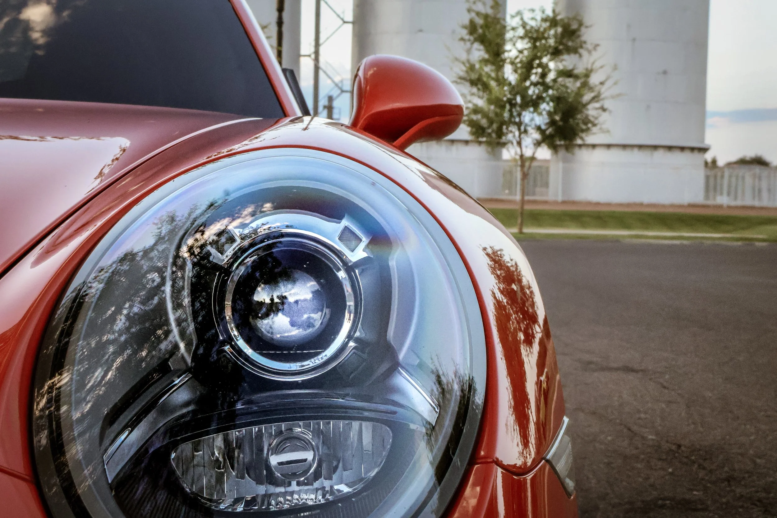 A super close shot of a single headlight of a Porsche 911 showcasing the details of the unit with the Morrison Ranch silos in the background.