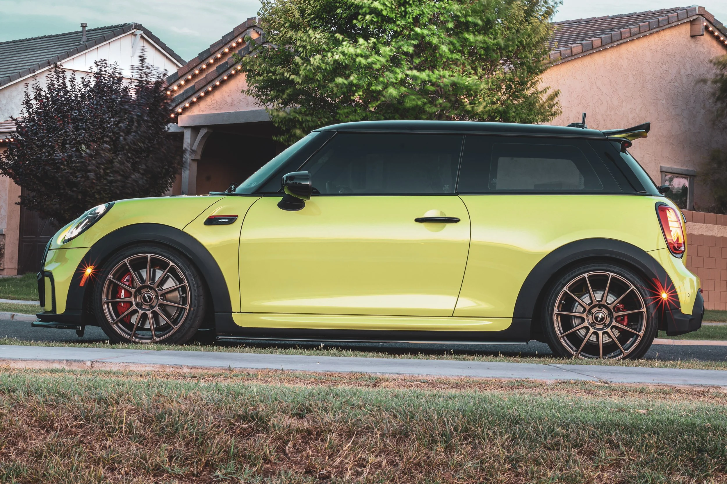 Side profile automotive photography featuring a vibrant yellow Mini Cooper JCW, highlighting the illuminated front and rear side marker reflectors and bronze wheels, parked on a residential street at dusk in Morrison Ranch, Gilbert, Arizona, Photosho